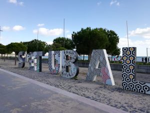 Buchstaben der Stadt Setúbal im Sand mit dem Meer im Hintergrund