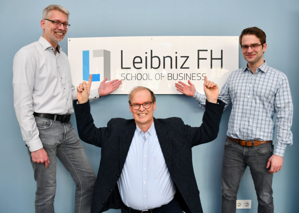 Gruppenfoto mit Holger Märtens, Uwe Groth und Robin Christmann vor dem Poster mit dem Logo der Leibnitz FH