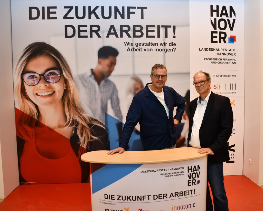 Prof. Gunnar Spellmeyer und Dr. Uwe Groth stehen am Stand der Landeshauptstadt Hannover, hinter Ihnen ein Aufsteller mit dem Aufdruck: "Die Zukunft der Arbeit"