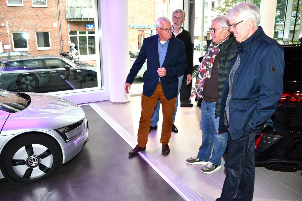 Die VDI-Kuratoriumsmitglieder stehen vor dem silbernen VW XL-1E im Ausstellungsraum und fachsimpeln über Elektromobilität.