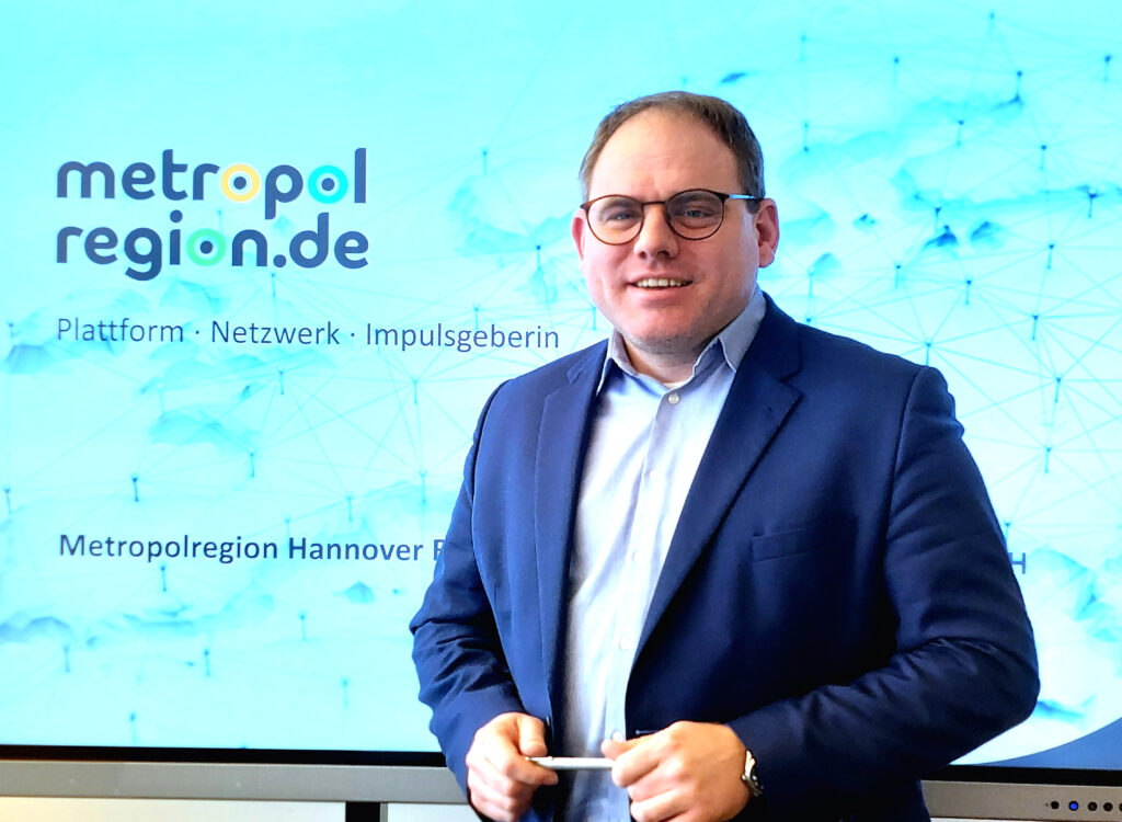 Christoph Meineke, Geschäftsführer der Metropolregion Hannover, vor einer blauen Leinwand mit einer Präsentation von der metropolregion.de