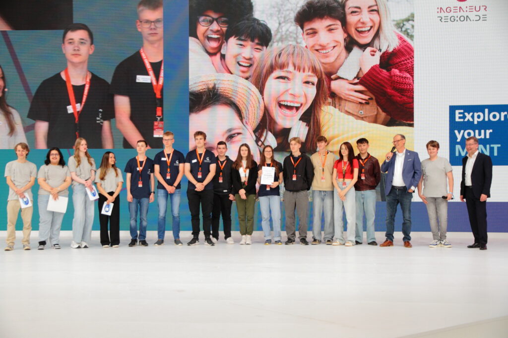 Die erstplatzierten mit dem Projekt "Parabolkraftwerk“ stehen gemeinsam mit den zweitplatzierten, Projekt „Wattamaran“, beide vom Berufsbildenden Gymnasium Georg-von-Langen-Schule in Holzminden und den Moderatoren auf der Bühne der Ideen Expo.